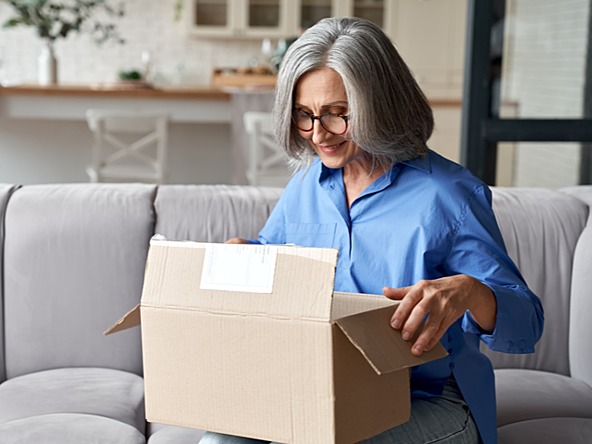 Woman opening cardboard box while sitting on couch